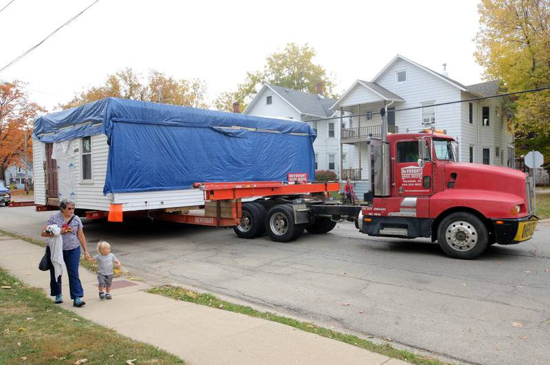 Curious onlookers walk along with a house being moved from the DeKalb County History Center property in Sycamore by Devooght House Movers as it makes its way down Pleasant Street in DeKalb Tuesday, Oct. 22, 2024, on its way to its new location in the 800 block of Pleasant in DeKalb. Habitat For Humanity is moving the house for Heaven Allen and her son who will be living in the home when it is completed.