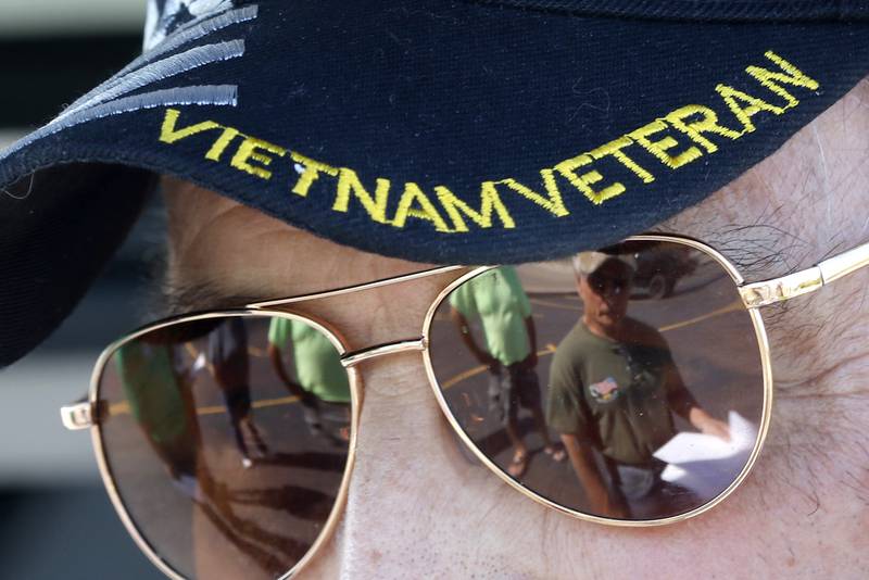 Volunteer Jim Garlic is reflected in the glasses of U.S. Army veteran Dan Klapperich, who served in the Vietnam War, as Klapperich explains the flag placing operation on Friday, May 26, 2023, at St. John the Baptist Cemetery, in Johnsburg.