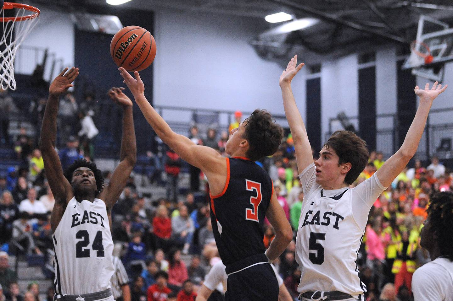 Oswego's Max Niesman (3) finger rolls a shot into the basket between Oswego East defenders Mekhi Lowrey (24) and Mason Blanco (5) during a boys’ varsity game at Oswego East High School on Friday, Dec. 9, 2022.