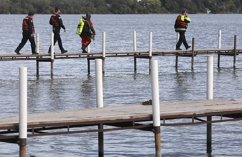 A diver walks the docks as a search team prepares to search an area as divers from the Antioch Fire Protection District and a sonar team from the Illinois Department of Natural Resources continue searching Tuesday, Oct. 7, 2025, on Fox Lake near Antioch for a man thrown from a boat he was test driving Monday night.