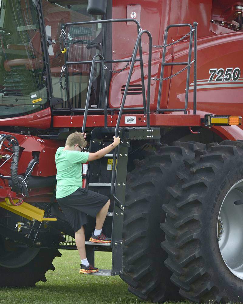 Corbin Haun carefully climbs up this Case combine Sunday, July 28, 2024, during the Touch A Truck event at Riverfront Park in Ottawa.