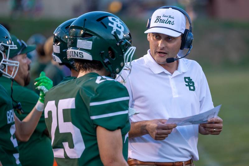 (from left) Brennan Hirst (25) of St. Bede talks with head coach Jack Brady on sideline during game on Friday, Sept 12, 2025 at Captain Thomas J. Heitmann field in Peru.