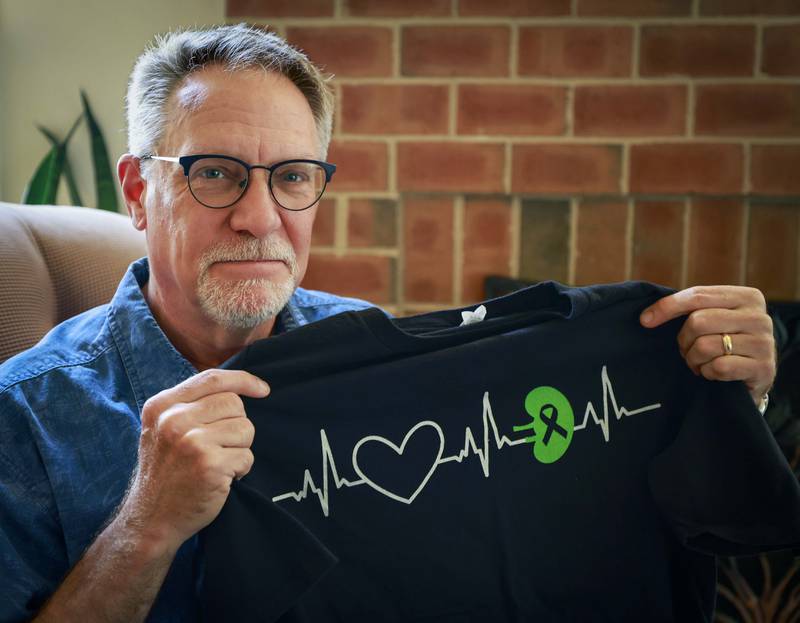 Mike Torti holds a kidney donor shirt Tuesday, June 10, 2025 at his house in Woodridge that his friends gave him. Torti donated his kidney via what is called a paired exchange to Jacob Fill, now 28, the son of a former Elmhurst neighbor who he hadn't seen in more than 20 years. Although Mike was a match, Fill's doctors determined that a younger donor would be preferable. Mike agreed to a paired donation where he donated a kidney to someone else so that Jacob could receive a kidney from a younger donor.