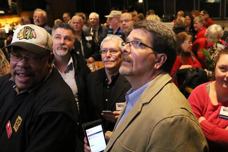 McHenry County Board member Chuck Wheeler (left) and McHenry County Clerk-elect Joe Tirio (right) look up at a TV broadcasting election results Tuesday inside a packed room at Bulldog Ale House in McHenry.