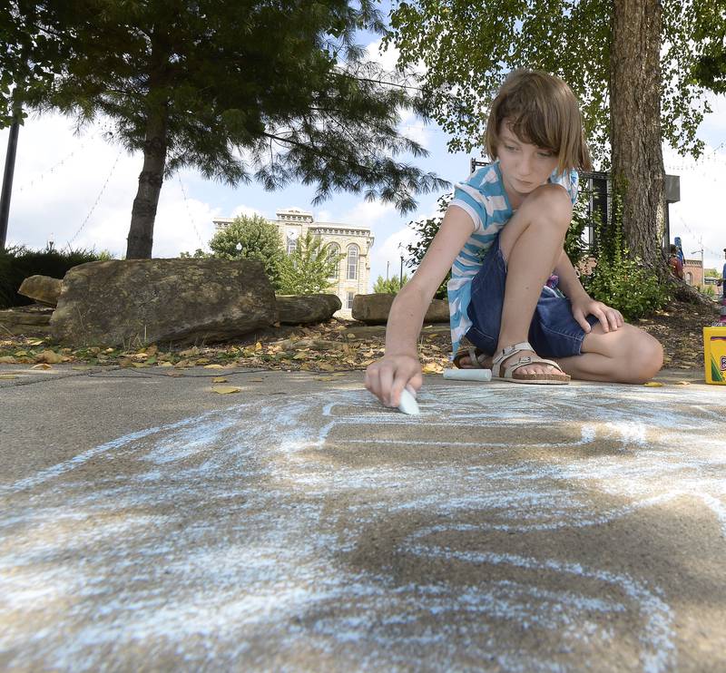 Serenity Seigler finds a shady spot Saturday, Aug. 6, 2022, at the Jordan block in Ottawa to create a chalk drawing as part of Kid’s Play Day.