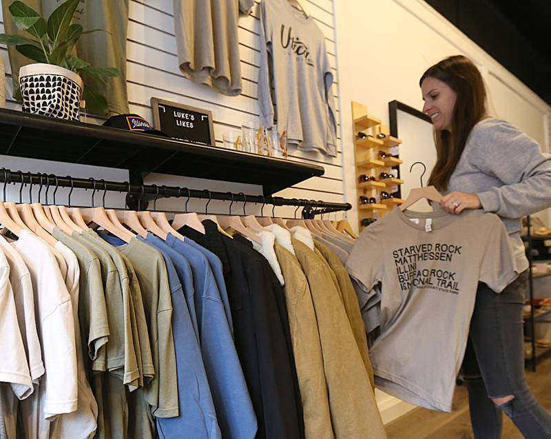 Kylie Mattioda owner of Wears Well holds displays a Starved Rock and Matthiessen shirt in her store on Monday, Dec. 19, 2022 in Utica.