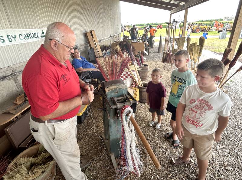 The Buckwalter brothers, Lincoln, Everett, and Baylor, from Geneseo, ages 9, 9, and 5, watch Carvel Morgan of Davenport make them a broom by hand, weaving different sizes, shapes and colors on his antique, not mechanized machinery at the Bos Family Farms on Friday, July 25, 2025.