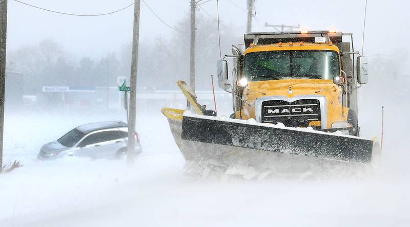 A snowplow travels by a vehicle in the ditch Monday, March 16, 2026, at the corner of Somonauk Road and Fairview Drive in Cortland. A March snowfall covered DeKalb County in about six inches of the white stuff Sunday night into Monday.
