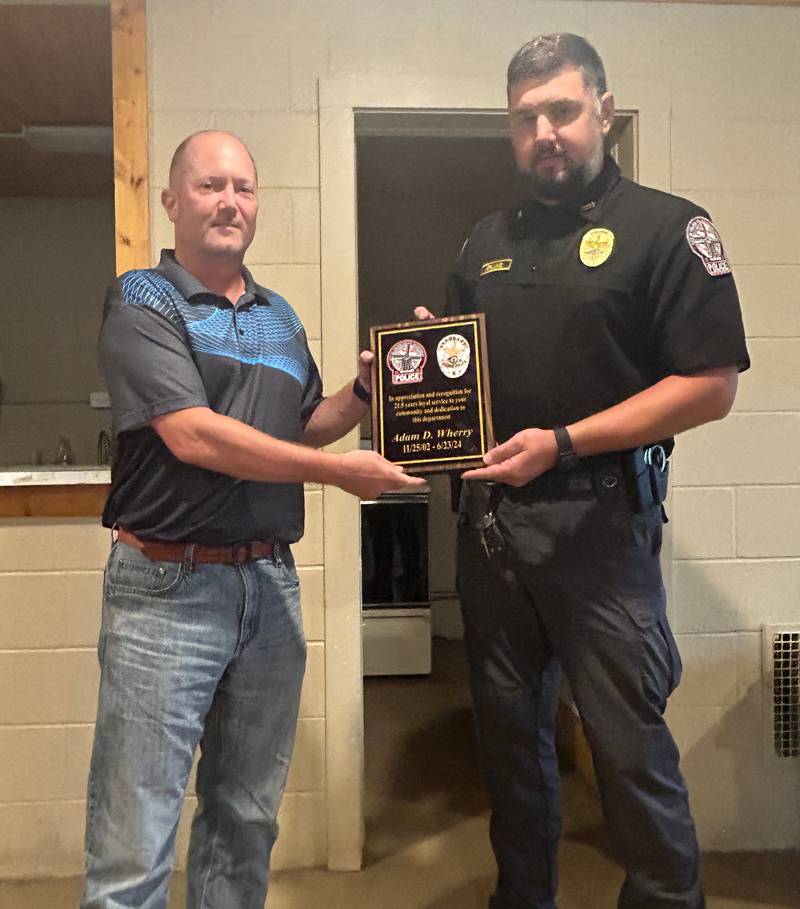 Fulton police officer Adam Wherry (left) receives a plaque from Fulton Police Chief Nick Neblung for his years of service to the department.