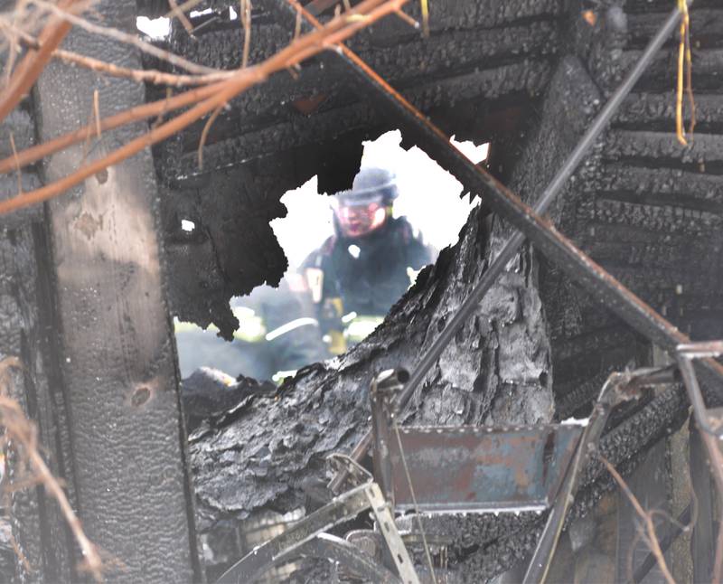 A firefighter can be seen through the charred remains of a garage at 6727 W. Henry Road, southeast of Polo, on Wednesday, March 26, 2025.