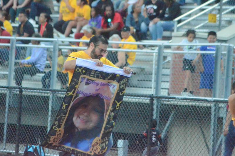 A man carries a poster remembering Abigail "Abi" Ayala at an East Aurora High football game against Streamwood on Friday, Sept. 12, 2025, to support Cal's Angels, a St. Charles-based nonprofit foundation dedicated to granting wishes, raising pediatric cancer awareness and funding research. Abi died in 2024, months after she was honored by the city of Aurora on World Cancer Day.
