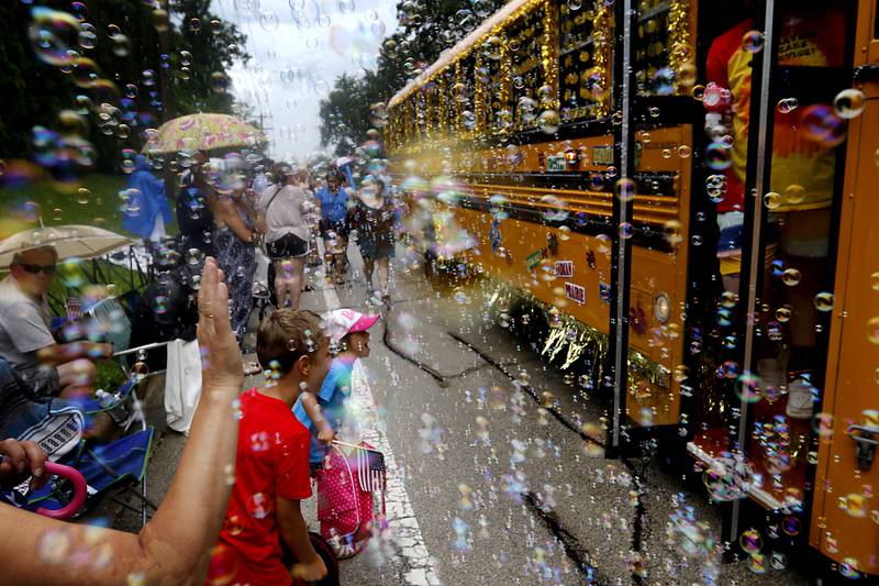 People wave and children react the the bubbles from a District 47 and 155 school bus on Sunday, July 7, 2024, during Crystal Lake’s annual Independence Day Parade on Dole Avenue in Crystal Lake. This year’s parade feature close to 100 units.