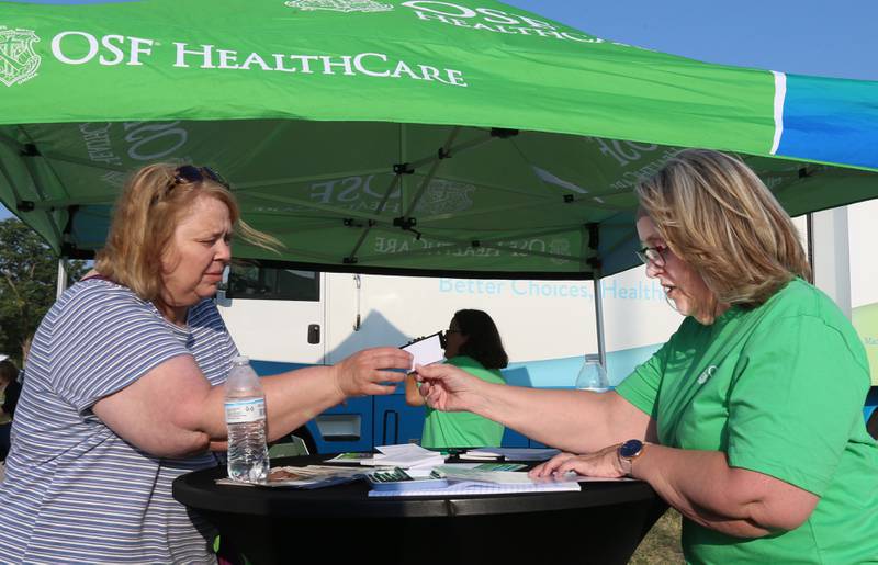 Anne Devert of Princeton, is handed a card with information by OSF Stephanie Eddens program manager for senior behavioral wellness during First Responder night at the Illinois Valley Pistol Shrimp baseball game at Schweickert Stadium on Tuesday, June 20, 2023 in Peru.
