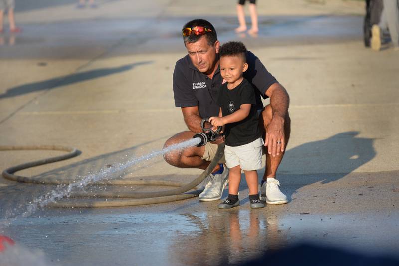 Kai Nwaokai, 2, of Dallas, Texas, uses a fire hose under the direction of Byron Firefighter Jayson Dimodica during one of the kids events at the Ogle County Sheriff's Department and Byron Police Department's National Night Out in Byron  on Tuesday, Aug. 5, 2025. Other agencies also took part in the evening event.