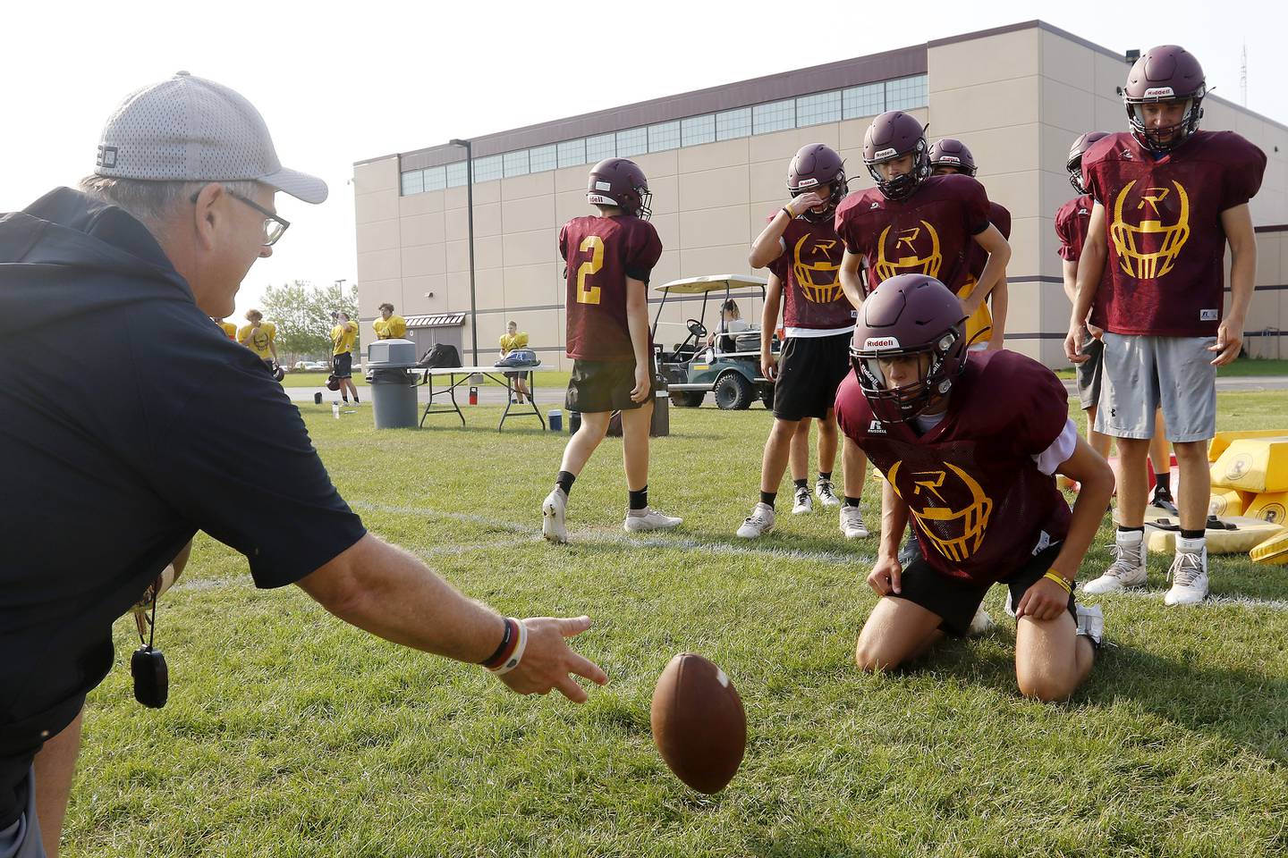 Coach Mike Noll, left, gently tosses the ball on the ground for Stephen Tower to smother during practice with the varsity football team at Richmond-Burton High School on Wednesday, July 14, 2021 in Richmond.