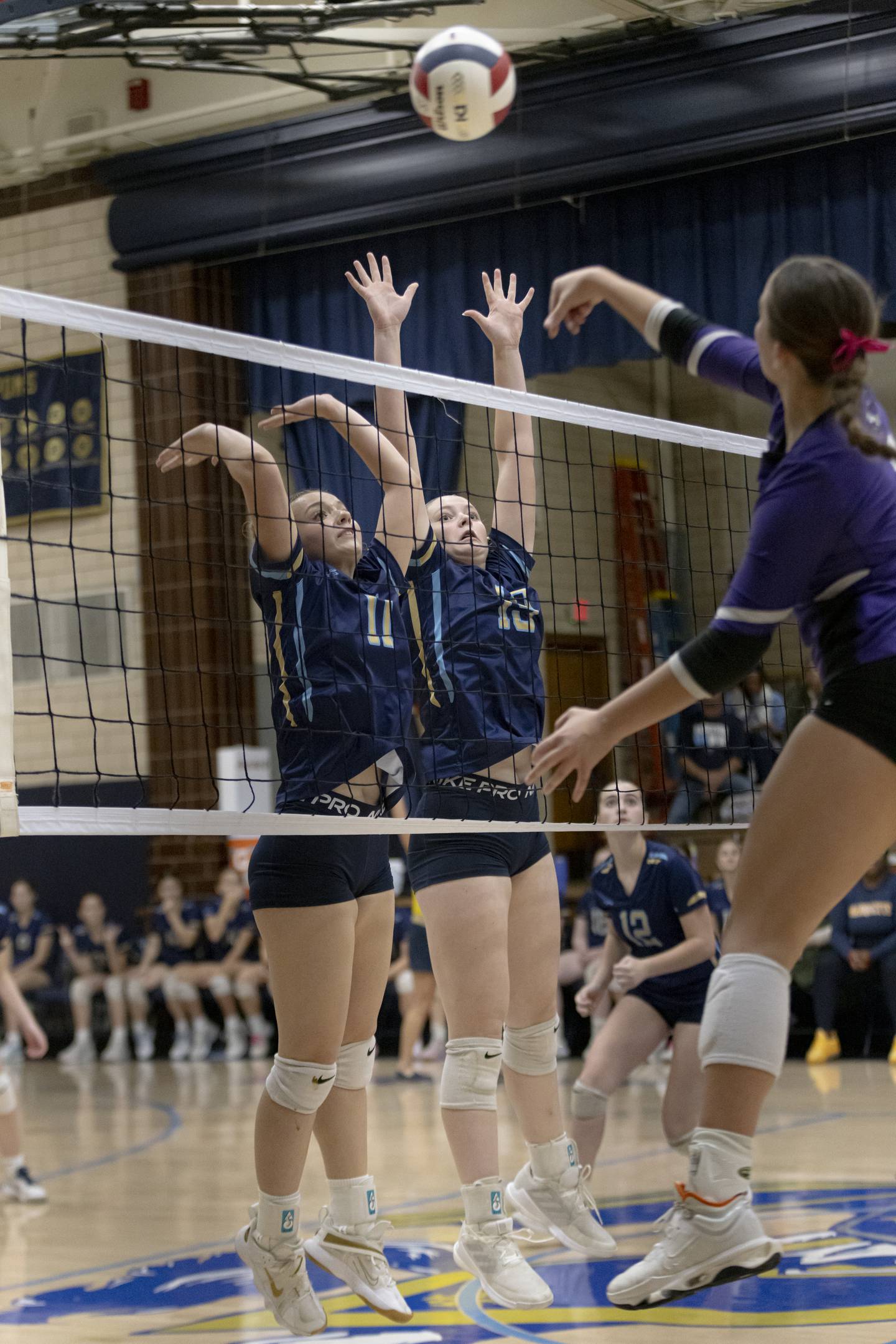 Ava Offermann (left) and Lilia Muffler (right) jump at the net to block a spike from a Lexington High School athlete during the Class 1A Sectional girls volleyball tournament at Bader Gym on November 5, 2024.