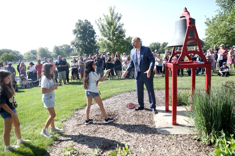 Louise White Elementary School Principal Kevin Skomer assists students as they ring the school bell on the first day of school in Batavia on Wednesday, Aug. 16, 2023.