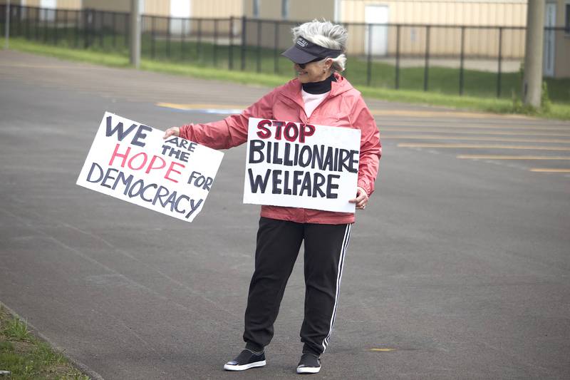 Kathy Mazur holds up signs on Thursday, May 1, 2025, for a democracy rally in Joliet with signs critical of U.S. President Donald Trump. More than 20 people attended the rally held near the busy West Jefferson Street and the Joliet Regional Airport.