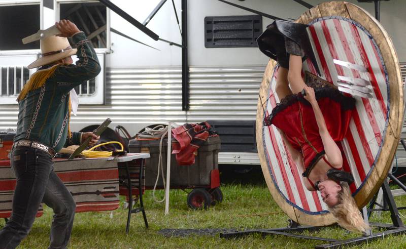 The Rhinestone Roper throws knives at his assistant as she spins on a wheel during a performance at the Ogle County Fair in Oregon on Thursday, July 31, 2025.