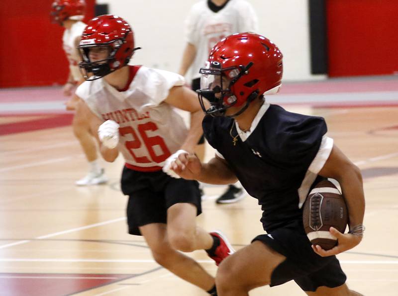 Huntley’s Sam Deligio runs with the ball during the first day of football practice Monday, 8, 2022, in the Huntley High School  field house after stormy weather move practice inside.