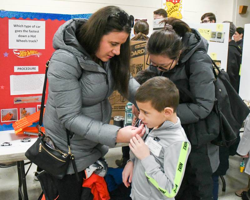 Dajana Randjelovic puts a button on her son Aleksandar Randjelovic that reads “I’m a 58 Scientist” during the Downers Grove District 58 science fair held at O’Neill Middle School in Downers Grove on Saturday Jan. 20, 2024.