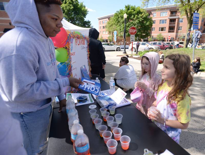 Dashaun Crawford with the Downers Grove YMCA offers a flavor challenge to children and adults including (left) Madelyn Harris and Kathryn Barbaro of Downers Grove  during the Downers Grove Farmers Market Saturday May 11, 2024.