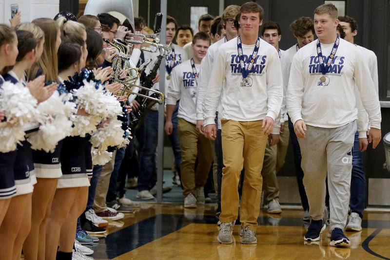 The Cary-Grove football team, led by quarterback Ben McDonald (left) and offensive lineman Addison West are serenaded by band members as they enter the school's lower gymnasium for a celebration of the Class 6A state championship Sunday in Cary.