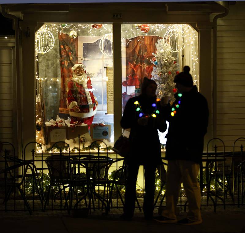 A couple wearing light up necklaces pauses in front of a Christmas display during the annual Christmas Walk with the arrival of Carolers, Santa Lucia and Santa Claus Friday, Dec. 6, 2024 in Geneva.