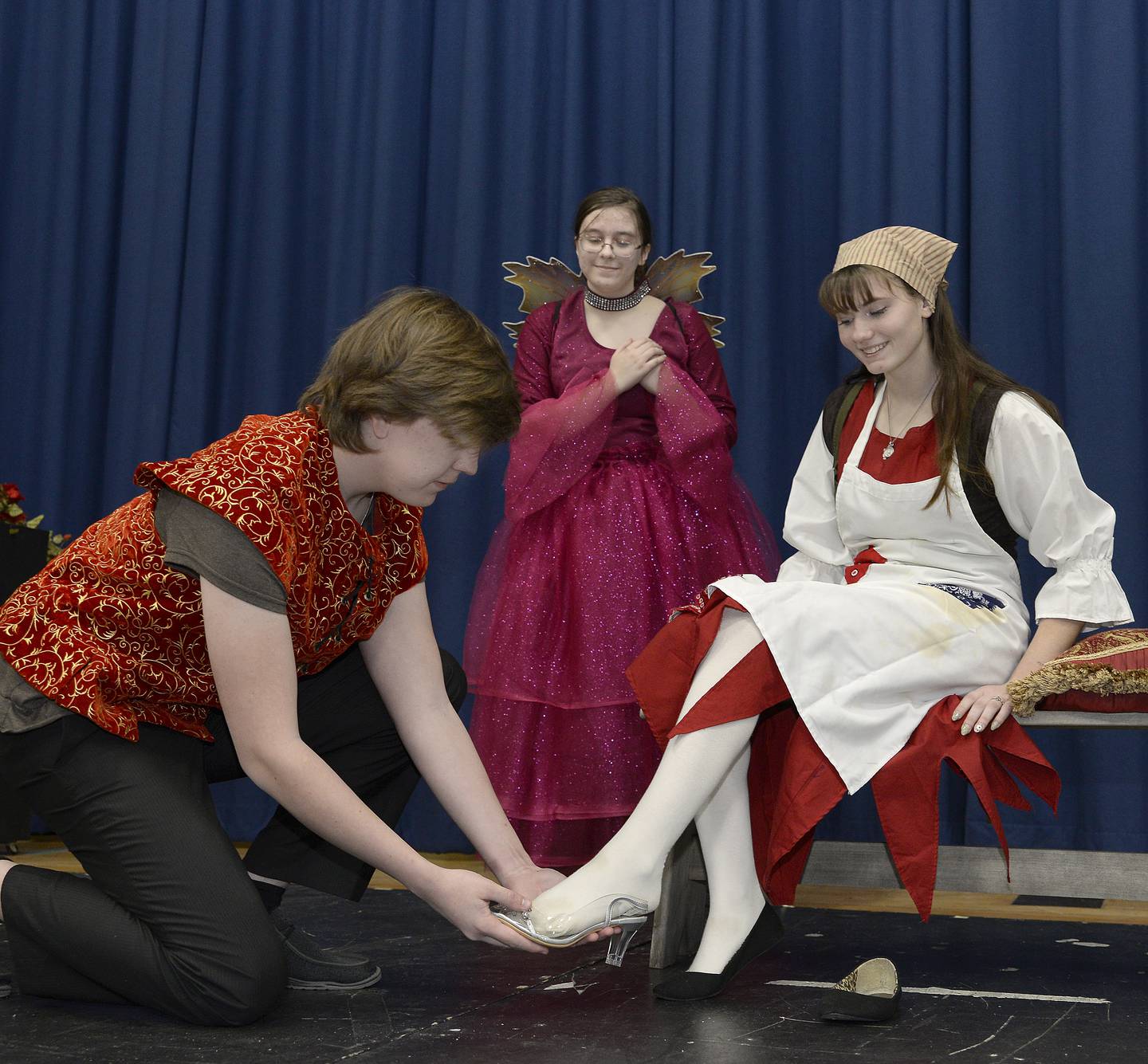 Marquette Academy students Jacob Witthuh as the Prince, tries a slipper on Ella Biggin as Cinderella, as Irene Vicich as the Fairy Godmother looks on in a scene from "Cinderella" that will be performed Friday, March 31, and Saturday, April 1, at the school.