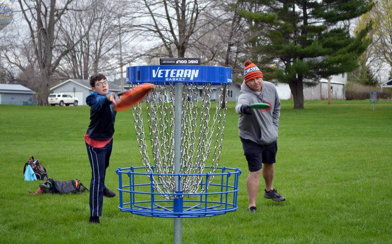 Corbin Martin, 14, and dad Andy Martin, both of Rockford, toss disc golfs discs toward the basket that serves as the sport's goal. Andy Martin grew up in Polo and has been disc golfing on-and-off for about 20 years; Corbin, has been playing for one year. The pair attended the grand opening of the disc golf course at Keator Park in Polo on May 1.