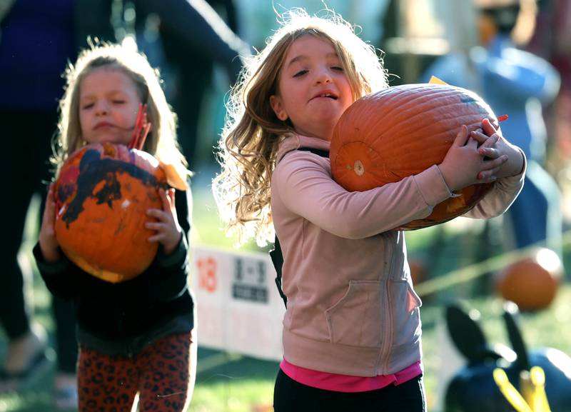 Grace Rex, (right) 8, from Sycamore and her sister Karen, 6, carry their pumpkins to their spot Wednesday, Oct. 23, 2024, on the DeKalb County Courthouse lawn during the Sycamore Pumpkin Festival.