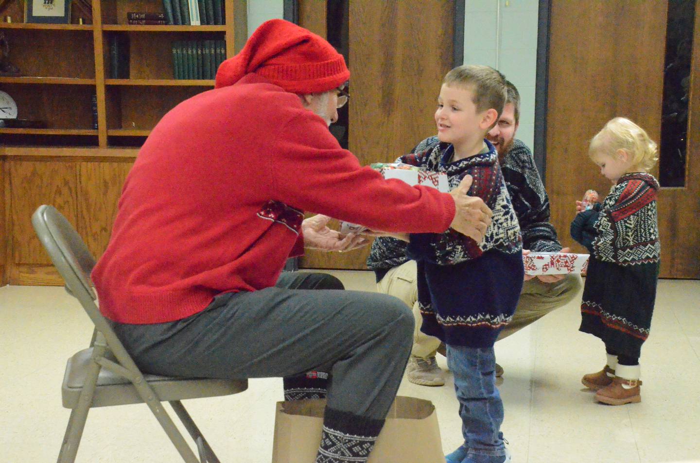 Norwegian Santa Julenisse, Ken Johnson of Yorkville, left, presents gifts to Archer Ruhl of North Aurora Sunday. Background are Archer's dad and sister Lucy. Julenisse's visit highlighted Sons of Norway Polar Star Lodge 5-472's annual Nordic-style yuletide party at St. Olaf Lutheran Church, Montgomery.