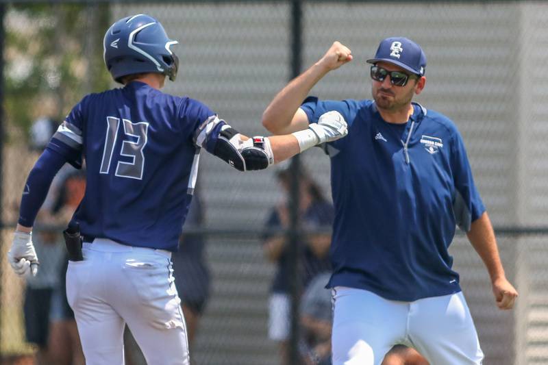 Oswego East's Cody Haynes (13) celebrates with head coach Brian Schaeffer after a successful bunt hit during Class 4A Romeoville Sectional final game between Oswego East at Oswego.  June 3, 2023.