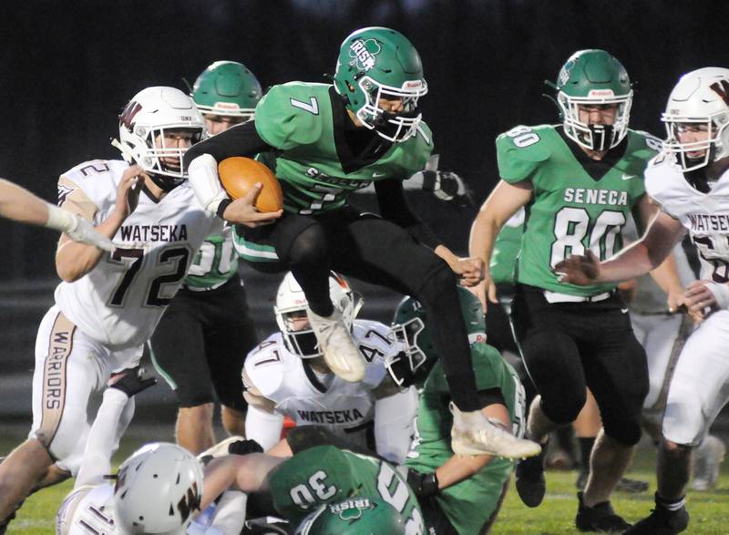 Seneca quarterback Nathan Grant (7) jumps over a block by teammate Cole Underhill (30) in the first half of Friday night's home game against Watseka.