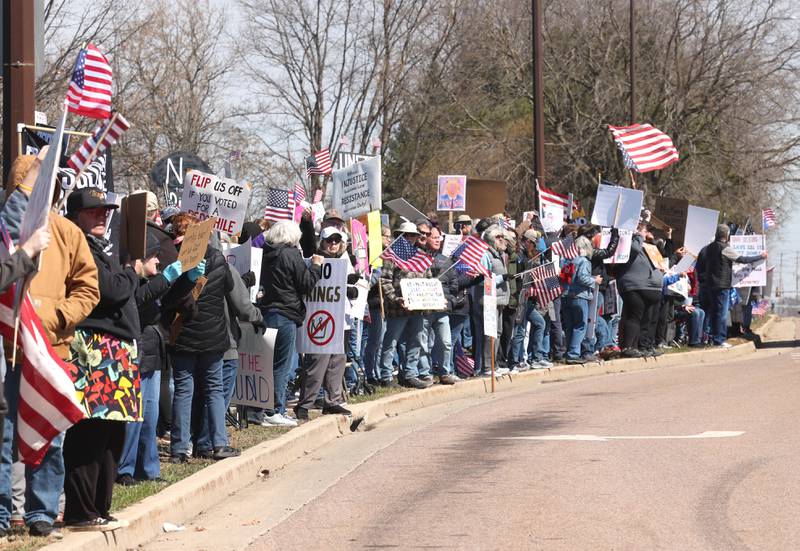 Protesters line Sycamore Road in front of Hopkins Park in DeKalb Saturday, March 28, 2026, during a No Kings march and rally against the federal actions of President Donald Trump and his administration.