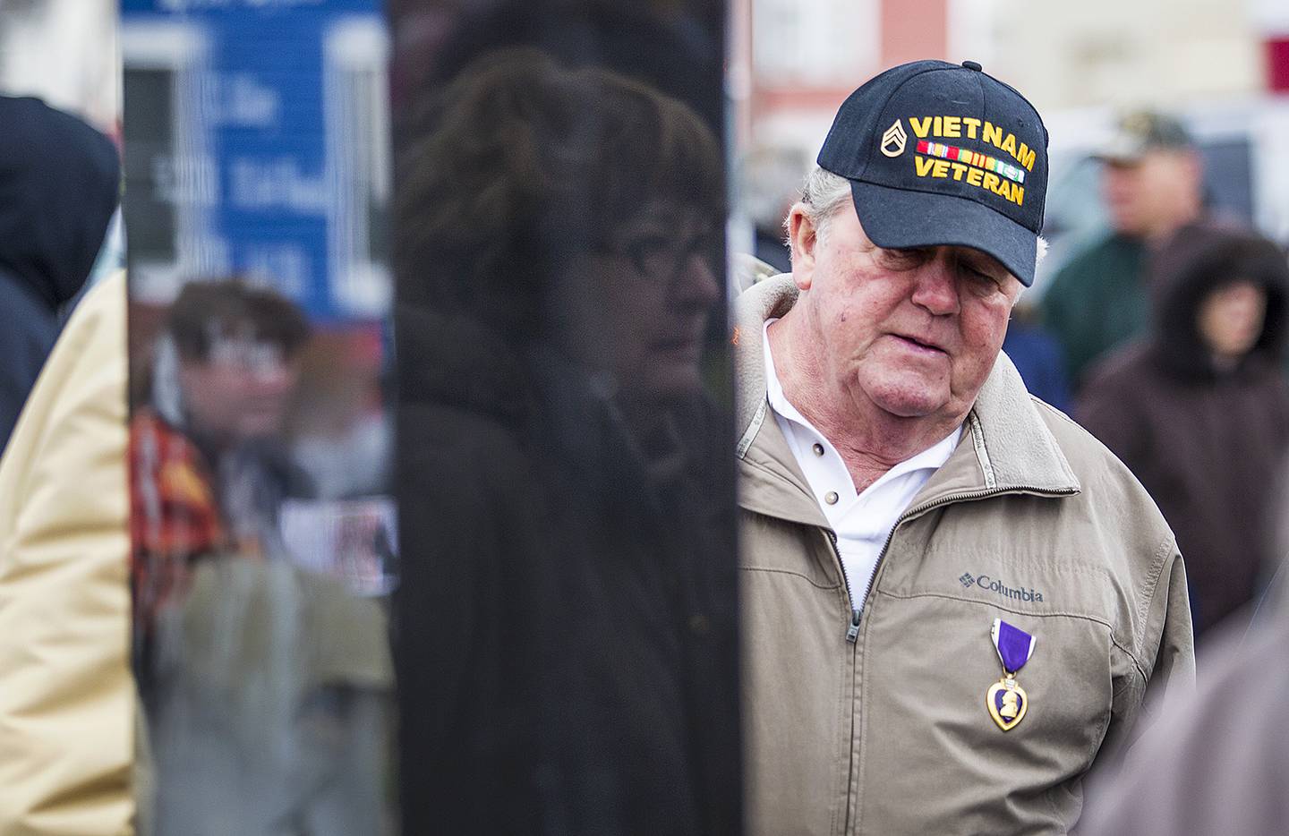 Jackie Raycraft (reflected) and Tom Bitterman look the new newly unveiled Vietnam War memorial in 2014 in McHenry. The monument was built in honor of four McHenry High School graduates killed in Vietnam. The memorialized included John Granath Jr., killed at 20; Glenn Davis, killed at 22; Carter Freund, killed at 22; and James Ambrose, killed at 23. Raycraft is the sister of Ambrose. Bitterman, family friend of Davis, signed his induction papers on the day Davis was killed.  Glenn Davis is now buried next to Bitterman's brother Dick Bitterman.