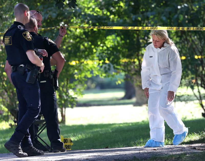 A DeKalb County sheriff’s deputy lifts the crime scene tape for an investigator in a protective suit Tuesday, Sept. 30, 2025, in front of a house in the 1300 block of Oakland Drive in Sycamore where two people were found dead Tuesday morning.