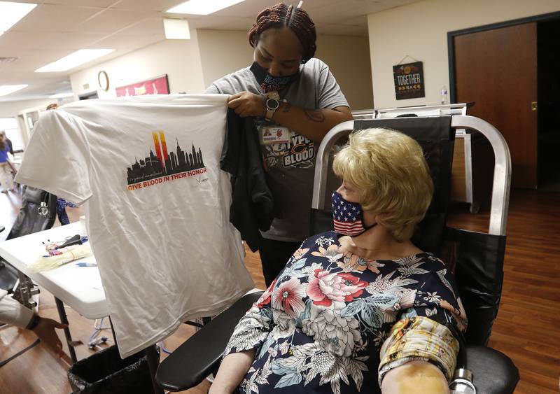 Versiti phlebotomist and team lead Asya Golston shows Laraine Kubiak, of McHenry, a free gift shirt reading "Give Blood In Their Honor" during the Meet a Hero Be a Hero blood drive with AmeriCorps Seniors, Senior Service Associates, and Versiti at McHenry Senior Center on Thursday, Sept. 9, 2021 in McHenry.  The blood drive booked all 24 appointments and offered donors a chance to meet some first responders from the Johnsburg Police Department and McHenry Township Fire Protection District as a remembrance on the 20th anniversary of the terrorism attacks on Sept. 11, 2001.
