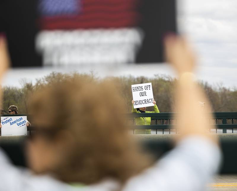 Protestors line the edges of the Galena Avenue bridge in Dixon Saturday, April 19, 2025, voicing their opinion of President Trump and their feelings the administration is not following a Democracy based government.