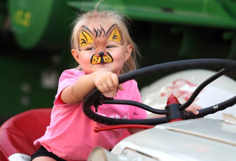 Raegan Parsons, 2, from Sycamore, climbs aboard one of the tractors on display Friday, Aug. 23, 2024, during the DeKalb Corn Fest.