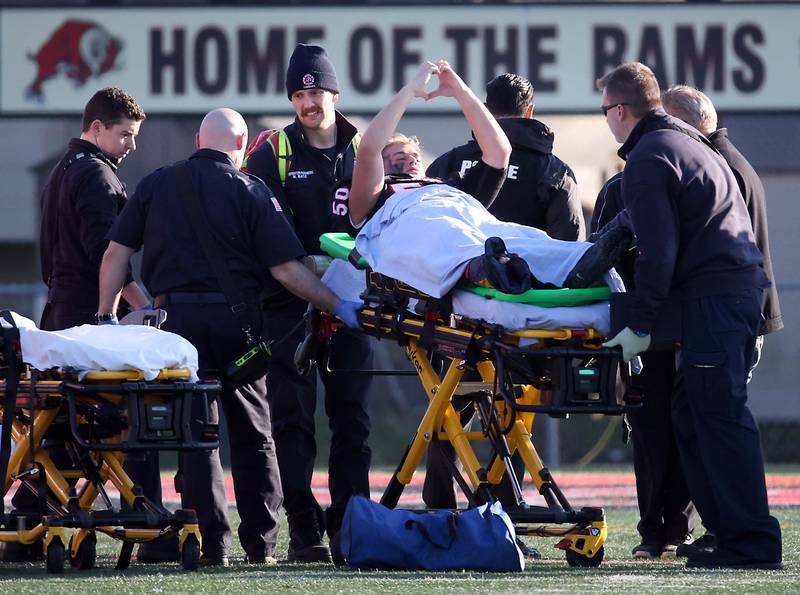 Glenbard East's Nathanial Schram (50) signals to the crowd as he is wheeled off the field on a stretcher  during the IHSA Class 7A quarterfinals Saturday November 11, 2023 in Lombard.