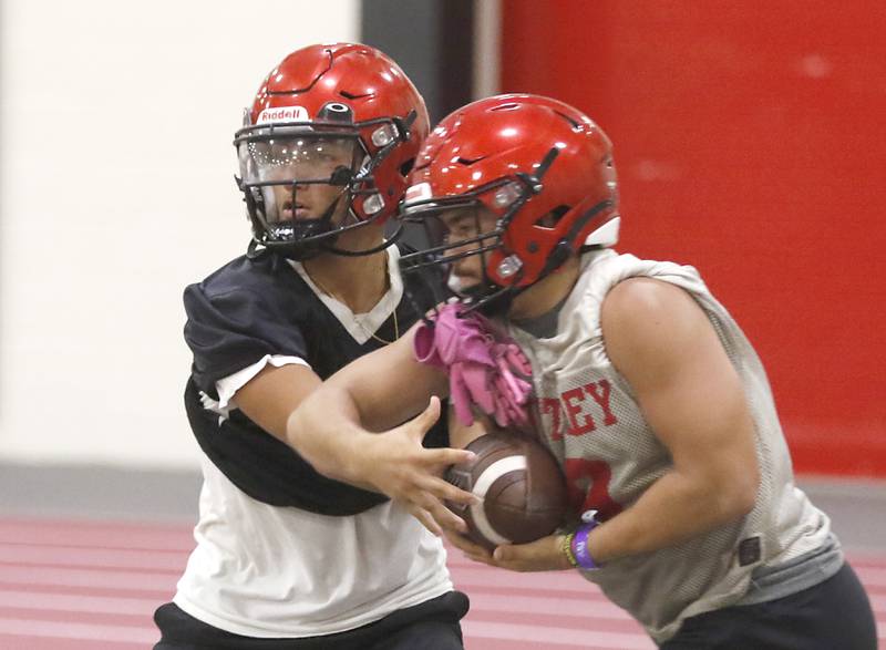 Huntley’s Sam Deligio hands the ball off to Zach Rios during the first day of football practice Monday, 8, 2022, in the Huntley High School  field house after stormy weather move practice inside.