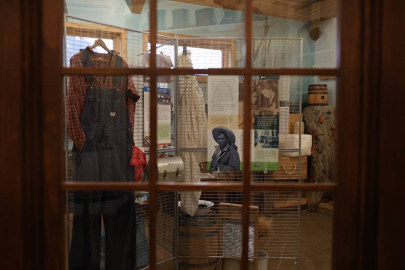 A display of 20th century history is seen through a window at the Isle a la Cache Museum “Journey Stories” exhibition in Romeoville.