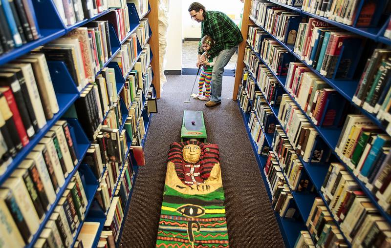 A Woodstock man helps his 3-year-old daughter to putt towards an obstacle in 2020 at the Woodstock Public Library. The 18-hole golf course weaves through the library and is open to golfers of all ages.