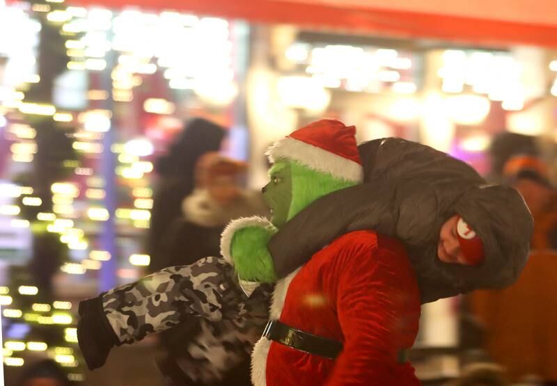 The Grinch totes a youngster through the streets during the Festival of Lights Holiday Parade in downtown Crystal Lake on Friday, Nov. 29, 2024.