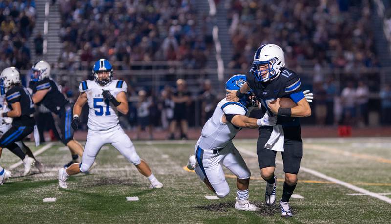 St. Charles North's Will Vaske (12) scrambles to avoid the pressure in the backfield from Lake Zurich's David Penaherrera (17) during a football game at St. Charles North High School on Friday, Sep 2, 2022.