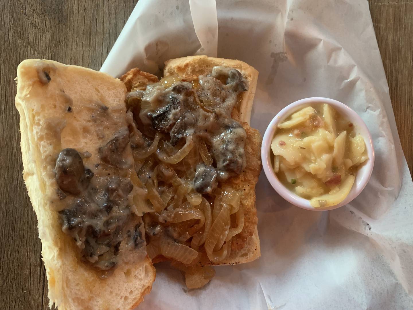 The Richmond Brat Haus Jaeger Schnitzel with mushroom gravy and grilled onions on a roll, with a side of warm German potato salad.