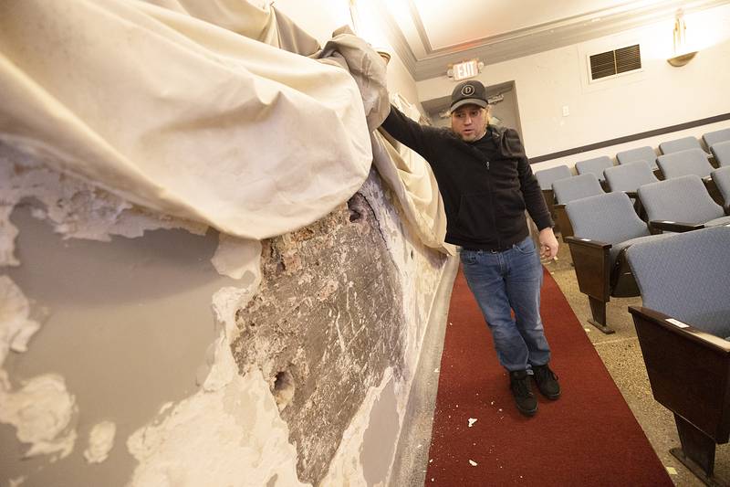 Scott Shipp holds a curtain that covers an extensively damaged south-facing wall Wednesday, March 6, 2024. Drainage from Peace Park and other structures has caused problems on the wall.