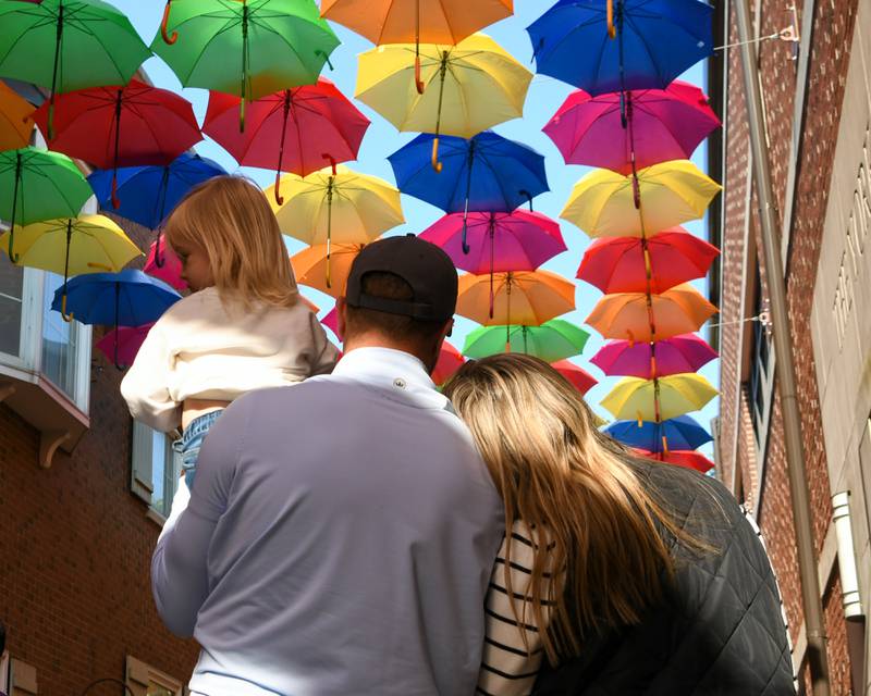 Ian Walker of Elmhurst holds his daughter Vivan Walker, 2, as his wife Allison Walker places her head on Ian’s shoulder for a brief moment as they enjoy the umbrellas over head on Schiller Court on Saturday May 31, 2025, during the Elmhurst Summer Kick Off Party held at City Centre Fountain Plaza in Elmhurst.