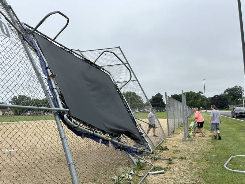 Three Byron School District employees work on removing a large trampoline that blew across N. Maple Street and was stuck on the backstop of a youth baseball field in Byron on Tuesday, July 16, 2024. A strong storm ripped that through the town Monday night.